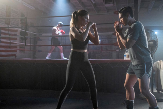 Ben and Addison shadow box in a dark gym in front of a hologram of two boxers