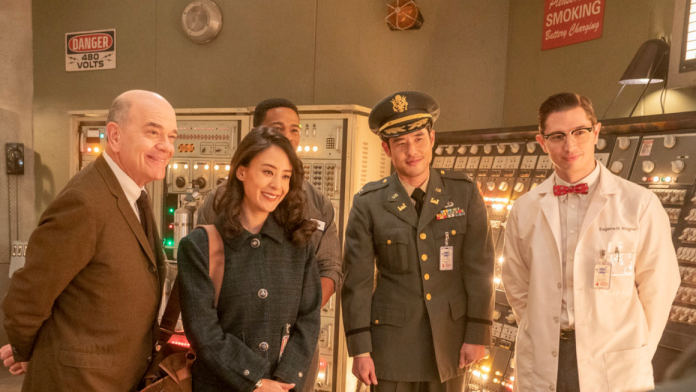 Dr. Woolsey, Mallory, Moe, Eugene, and Ben as the Colonel stand and smile in a nuclear reactor control room